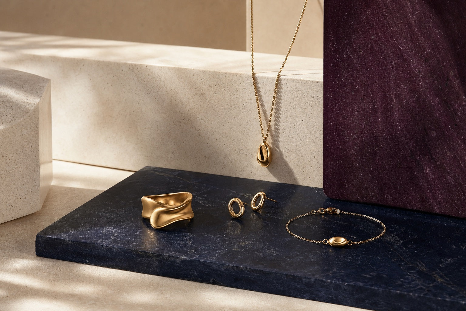 A curated yellow-gold jewelry still life on ivory, navy, and aubergine stone